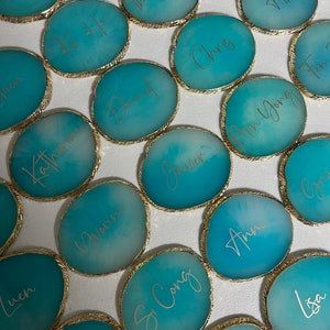 May include: A collection of teal blue agate coasters with gold trim and names written in gold script. The names include: Michael, Ka Ho, Daniel, Katherine, Javier, Chris, Alice, Min Yong, Si Cong, Ann, Jason, Luen, You Feng, and Lisa.