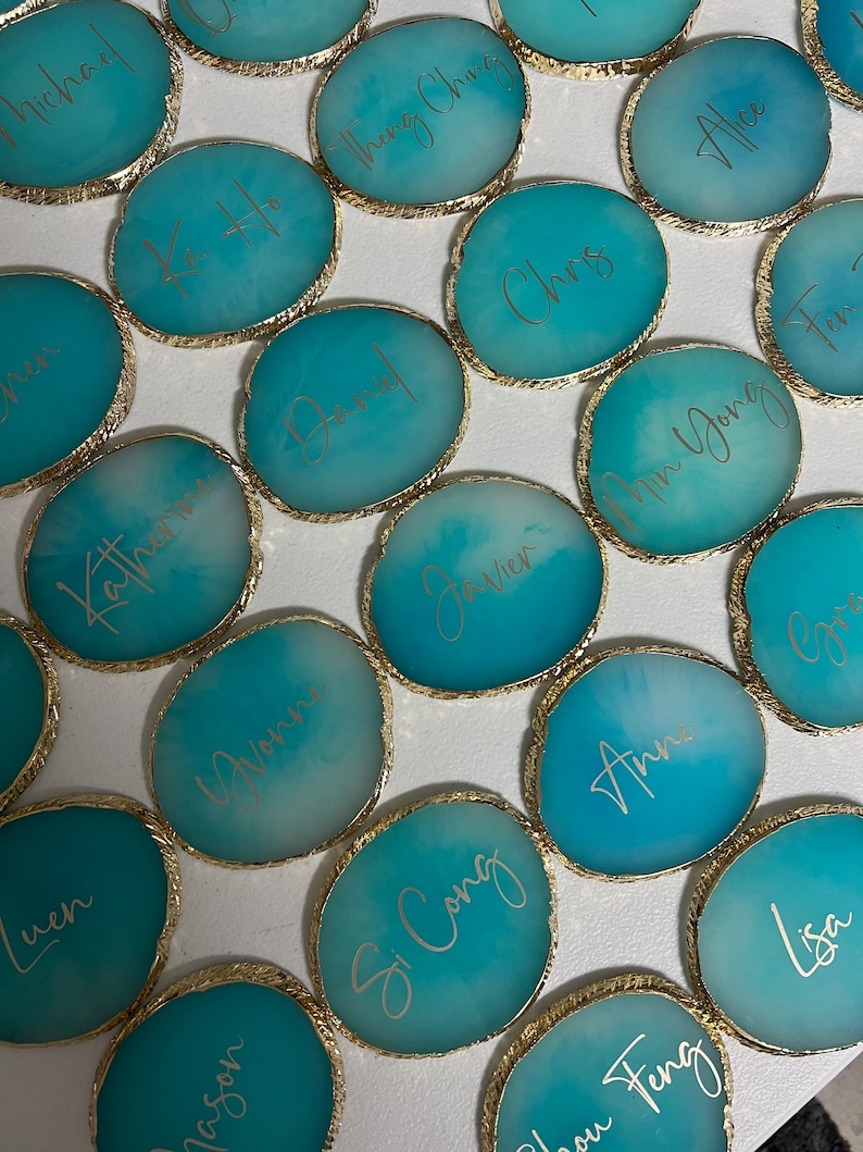 May include: A collection of teal blue agate coasters with gold trim and names written in gold script. The names include: Michael, Ka Ho, Daniel, Katherine, Javier, Chris, Alice, Min Yong, Si Cong, Ann, Jason, Luen, You Feng, and Lisa.