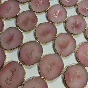 May include: Pink and gold round coasters with gold trim and names written in gold script. The names include Jem, Naomi, Temen, Ayla, Atahar, Claudia, Emir, Ueliz, Kerem, &Ouml;zkan, Elif, Halise, Tagu, Amara, Ilix, and Jennet.