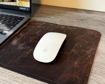 May include: A brown leather desk mat with a white wireless mouse on top. The mat has a distressed look and is designed to protect your desk surface.