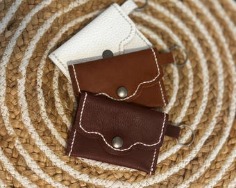 May include: Three leather keychains with scalloped edges and metal rings. The keychains are brown, white, and dark brown.