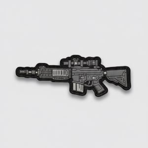 May include: A detailed patch featuring a stylized rifle with a scope and various attachments. The patch is primarily gray and black, with a textured appearance. The design is a tactical or military-themed item.