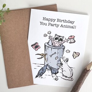 K&ouml;nnte beinhalten: Eine Geburtstagskarte mit einem Waschb&auml;ren in einem M&uuml;lleimer, einer Ratte und zwei Raben. Die Karte lautet "Happy Birthday You Party Animal!"