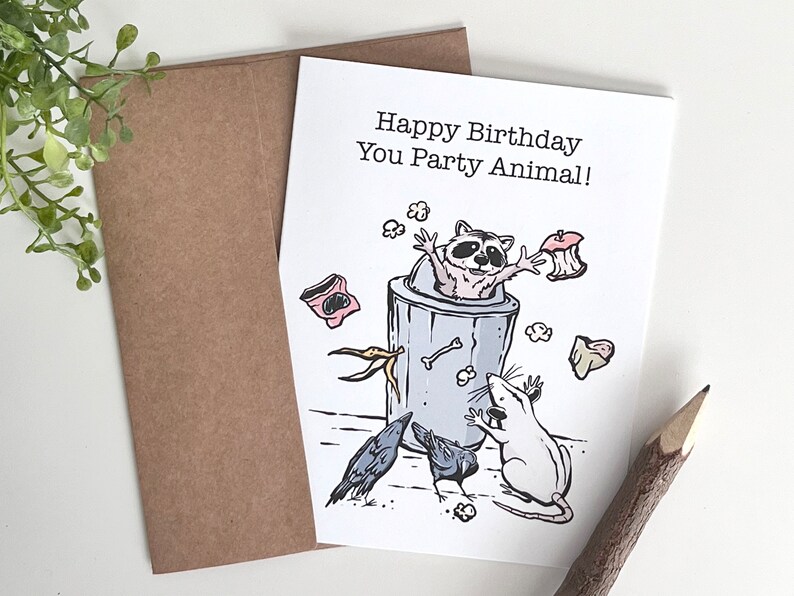 K&ouml;nnte beinhalten: Eine Geburtstagskarte mit einem Waschb&auml;ren in einem M&uuml;lleimer, einer Ratte und zwei Raben. Die Karte lautet "Happy Birthday You Party Animal!"