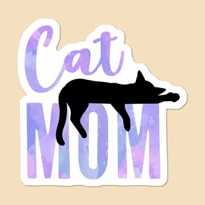 May include: A white sticker with a purple and blue watercolor background. The text "Cat Mom" is written in a cursive font with a black silhouette of a cat sleeping on top of the word "Mom".