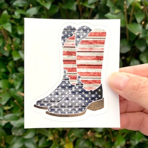K&ouml;nnte beinhalten: Ein Paar Cowboystiefel mit einem abgenutzten amerikanischen Flaggenmuster. Die Stiefel sind blau, rot und wei&szlig; mit einer Holzmaserung.