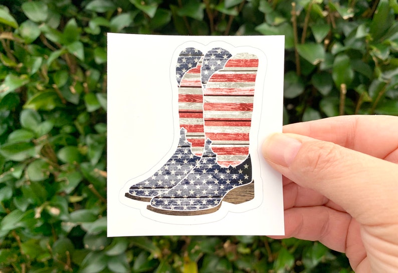 K&ouml;nnte beinhalten: Ein Paar Cowboystiefel mit einem abgenutzten amerikanischen Flaggenmuster. Die Stiefel sind blau, rot und wei&szlig; mit einer Holzmaserung.