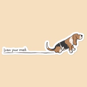 May include: A sticker featuring a cartoon Basset Hound dog in brown, black, and white, with the text "Leave your mark." The dog is sitting, with a line extending from its rear. The background is a solid beige color.