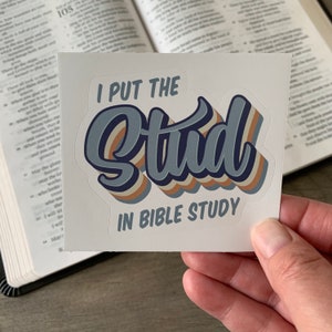 May include: A white sticker with the text "I put the stud in bible study" in a retro font. The word "stud" is in blue with orange and brown accents.