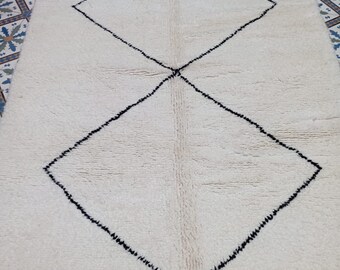 May include: A white Moroccan rug with a black diamond pattern. The rug has a fringe border.