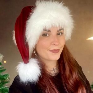 May include: A red Santa hat with a white fluffy trim and pom-pom. The hat is made of a soft, velvety material. The hat is a festive accessory for the Christmas season.