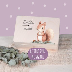 Könnte beinhalten: Helle Holzbox mit einer Eichhörnchen-Illustration. Auf dem Deckel stehen der Name "Emilia" und das Datum "29.03.2025". Ein lila Oval mit dem Text "6 TIERE ZUR AUSWAHL" ist ebenfalls auf der Box zu sehen.