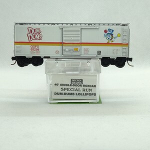 May include: A silver model train boxcar with red and yellow stripes and a Dum-Dums lollipop logo. The boxcar is labeled "40' Single-Door Boxcar Special Run Dum-Dums Lollipops".