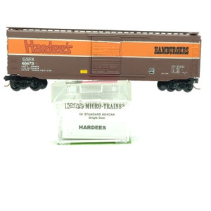 May include: A brown and orange model train boxcar with the words "Hardee's" and "Hamburgers" printed on the side. The boxcar is a 50' standard boxcar with a single door. The boxcar is made by Kadee Micro-Trains.