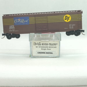 May include: A brown and yellow boxcar model train with the words "Crown Royal" and "DF" printed on the side. The model train is in a clear plastic box with the words "Kadee MICRO-TRAINS 50' STANDARD BOXCAR Single Door CROWN ROYAL" printed on the box.