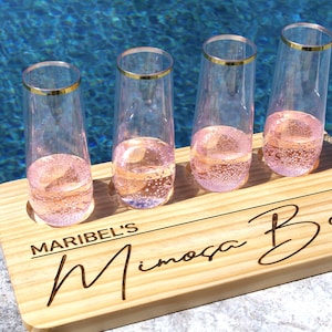 May include: Wooden serving tray with four champagne flutes filled with pink mimosa. The tray has the text "Maribel's Mimosa Bar" engraved on it.