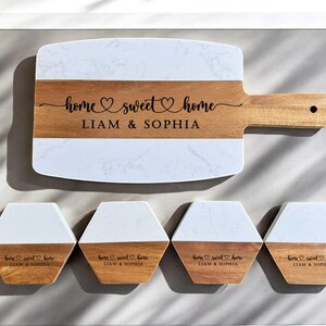 May include: A set of four white and wood coasters with the text "home sweet home Liam & Sophia" engraved on each. The set also includes a larger serving board with the same text.