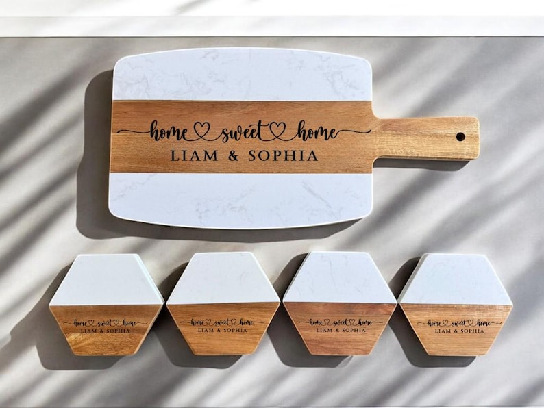 May include: A set of four white and wood coasters with the text "home sweet home Liam & Sophia" engraved on each. The set also includes a larger serving board with the same text.