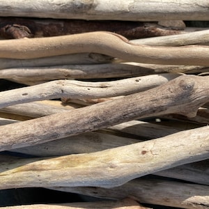 May include: Close-up of a pile of weathered driftwood pieces. The wood varies in color from light tan to grey, with visible textures and knots. The natural, organic shapes of the driftwood are arranged in a layered composition.