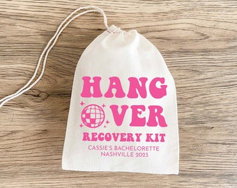 May include: White cotton drawstring bag with pink text that reads "Hangover Recovery Kit" with a pink disco ball graphic. The text below the graphic reads "Cassie's Bachelorette Nashville 2023".
