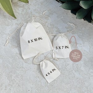 three white tote bags with measurements printed on them, placed on a textured surface.