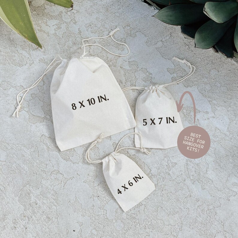 three white tote bags with measurements printed on them, placed on a textured surface.