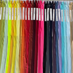 Peut inclure: Une collection de 40 tirettes de fermeture éclair de différentes couleurs, notamment le vert, le bleu, le jaune, l'orange, le rouge, le rose, le violet, le gris, le beige et le blanc. Les tirettes de fermeture éclair sont disposées en rangée, chaque couleur étant étiquetée avec une étiquette blanche.