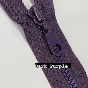 May include: A dark purple zipper with a metal slider and a pull tab. The zipper is closed and the teeth are visible.