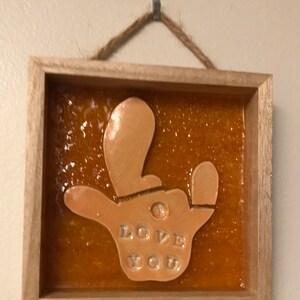 May include: A wooden framed wall art piece with a hand-shaped resin sculpture inside. The sculpture is orange and has the words "I LOVE YOU" embossed on it.