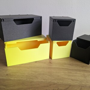 May include: Five small storage boxes, two are black and three are yellow. The boxes are stacked on top of each other.