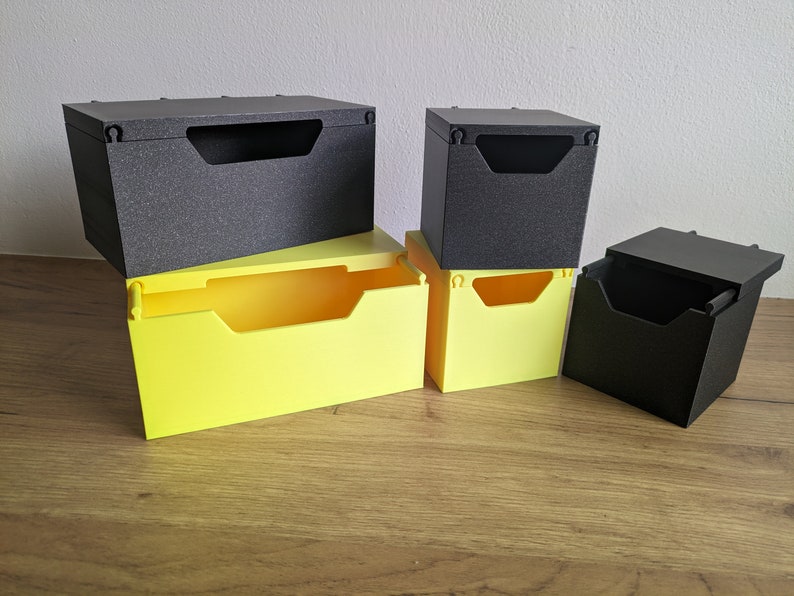 May include: Five small storage boxes, two are black and three are yellow. The boxes are stacked on top of each other.