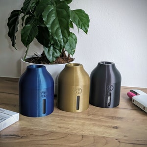 May include: Three ceramic diffusers in blue, gold, and black. The diffusers are cylindrical with a rounded top and bottom. They have a small opening on the top and a vertical slot on the side. The diffusers are sitting on a wooden surface.