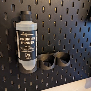 May include: A clear plastic bottle of Vallejo Airbrush Thinner, labelled "Airbrush Thinner 71.161 Diluyente Aerografo Verd&uuml;nnungsmittel" with the Vallejo logo. The bottle is hanging on a black pegboard.