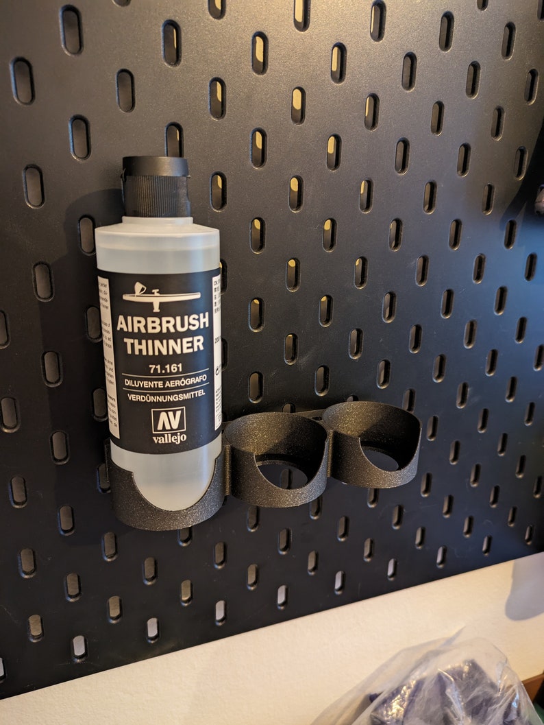 May include: A clear plastic bottle of Vallejo Airbrush Thinner, labelled "Airbrush Thinner 71.161 Diluyente Aerografo Verd&uuml;nnungsmittel" with the Vallejo logo. The bottle is hanging on a black pegboard.