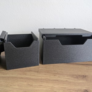 May include: Two black plastic storage boxes with lids. The boxes are open and have dividers inside. The boxes are on a wooden surface.