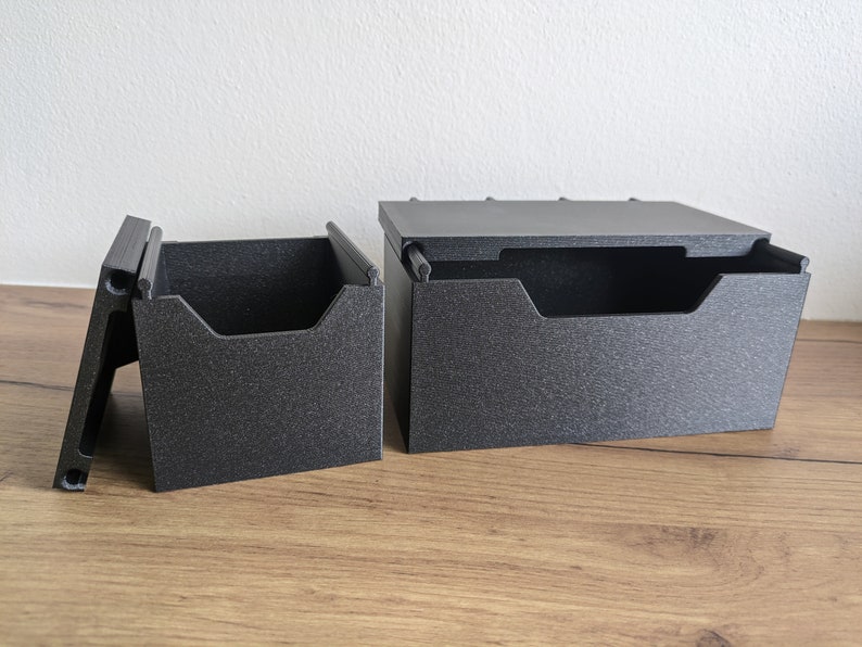 May include: Two black plastic storage boxes with lids. The boxes are open and have dividers inside. The boxes are on a wooden surface.