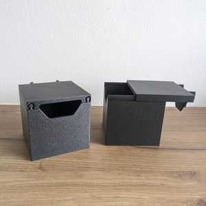 May include: Two black square boxes with lids. One box has a lid that is open and the other box has a closed lid.
