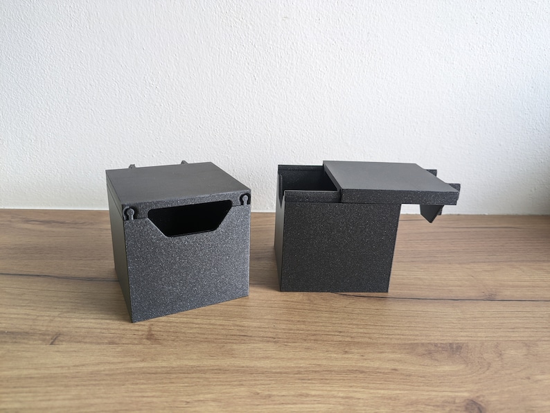 May include: Two black square boxes with lids. One box has a lid that is open and the other box has a closed lid.