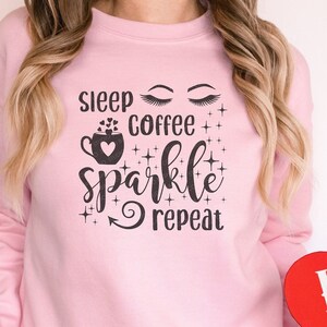 May include: A pink sweatshirt with the text "sleep coffee sparkle repeat" and a coffee cup graphic. The person is holding a red heart-shaped box with the word "LOVE" printed on it.