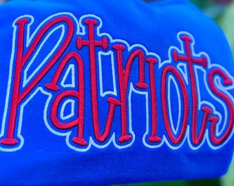 May include: Royal blue sweatshirt with the word "Patriots" in red, outlined in white. The text is in a cursive, stylized font. The sweatshirt is made of a soft material.