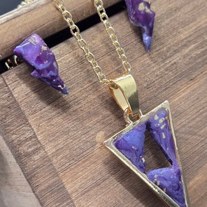 Peut inclure: Un collier en chaîne dorée avec un pendentif triangulaire violet et des boucles d'oreilles assorties. Le pendentif et les boucles d'oreilles ont un design marbré violet et or.
