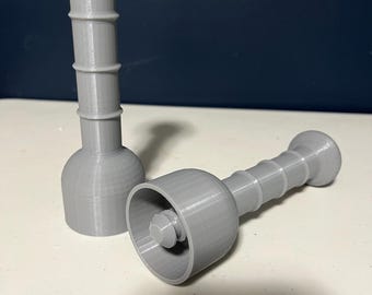 May include: Two gray, 3D-printed bottle stoppers. Each stopper has a bulbous top, a ridged cylindrical body, and a flared base. One stopper is upright, while the other is lying on its side, revealing its interior.