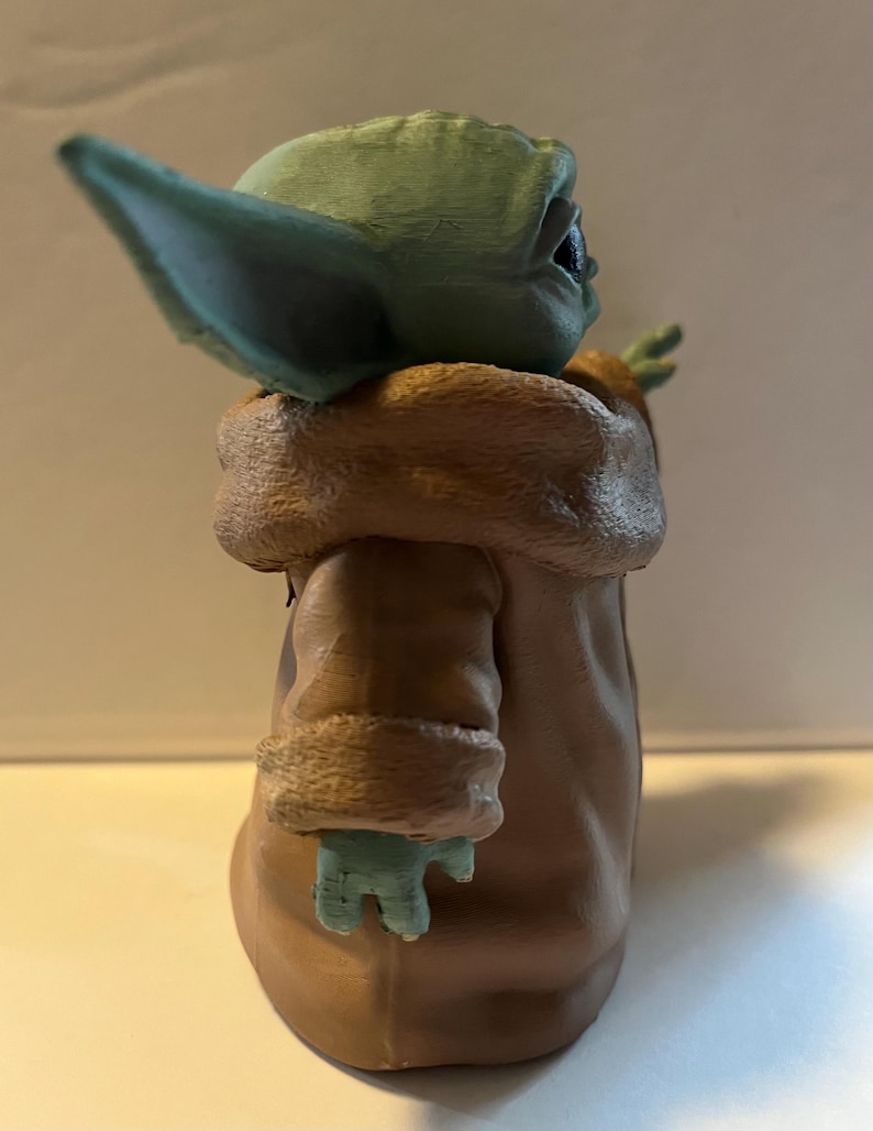 May include: A figurine of a character with large ears, green skin, and a brown coat with a fur-like collar. The figure is posed with one arm raised. The figurine is a collectible item.