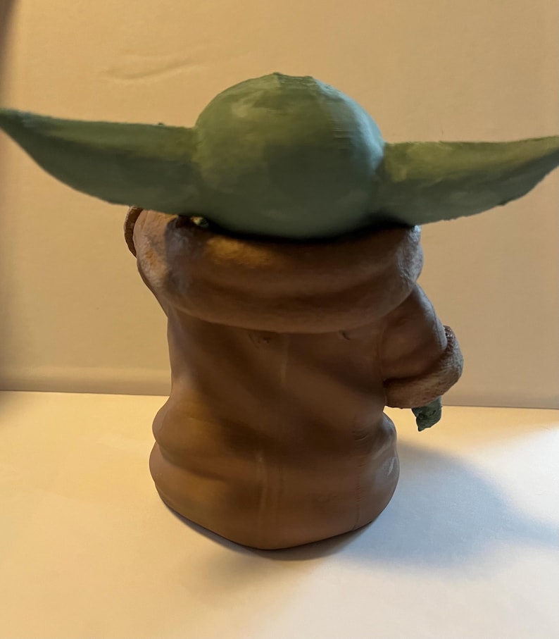 May include: A green-skinned character figurine with large ears, wearing a brown robe with a furry collar. The figurine is a stylized representation of a popular science fiction character.