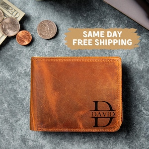 May include: A brown leather wallet with the name "DAVID" and the letter "D" engraved on the front. The wallet is rectangular and appears to be new. The background includes U.S. currency and coins.