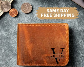 May include: A brown leather wallet with the name "VICTOR" and the letter "V" engraved on the front. The wallet is rectangular and has a worn appearance. The background includes U.S. currency and coins.