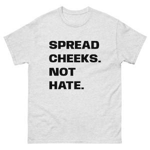 Può includere: T-shirt grigio chiaro con la scritta "SPREAD CHEEKS. NOT HATE." in grassetto nero. La maglietta ha un girocollo e maniche corte. Il tessuto sembra morbido e confortevole.