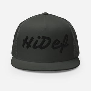 Può includere: Cappellino da camionista verde scuro con la scritta "HiDef" ricamata in nero. Il cappellino ha un retro in rete e una visiera piatta. Un accessorio classico e casual.