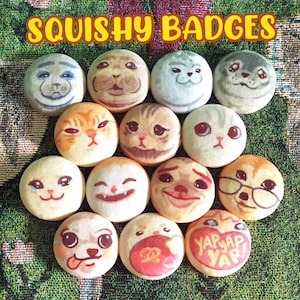 Pode incluir: Uma coleção de distintivos redondos e macios com vários rostos de animais, incluindo focas e gatos. Os distintivos são em tons de branco, bege e laranja, com expressões faciais detalhadas. O texto "SQUISHY BADGES" é exibido em amarelo.