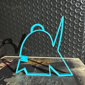 May include: A light blue plastic cookie cutter in the shape of a detective's hat and coat. The cutter is resting on a book with the title "THE GRAVE". The background is a textured black surface.